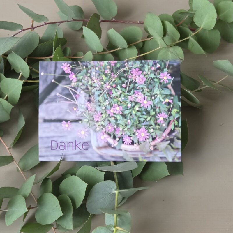 Blumenstrauß mit rosa Blüten auf einer Karte mit dem Wort „Danke“ auf einem Eukalyptus-Hintergrund.