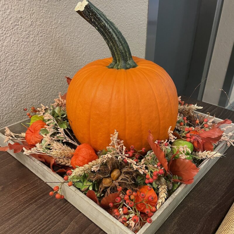 Kürbis-Deko mit Herbstlaub und Beeren in Holzkiste auf Tisch, ideal für herbstliche Stimmung.