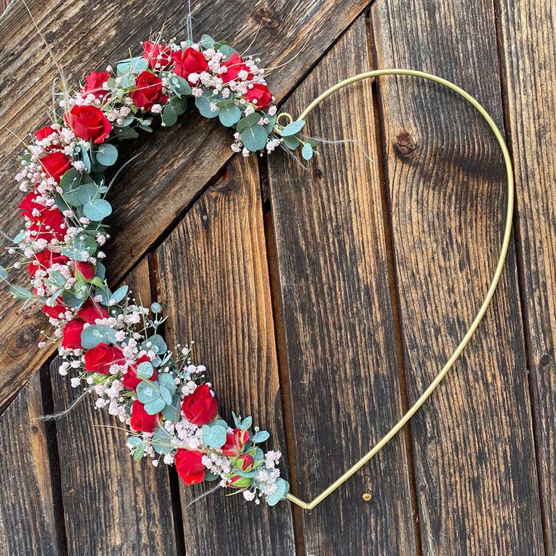 Herzförmiger Kranz mit roten Rosen und Eukalyptus auf Holzhintergrund: Romantische Deko-Idee.